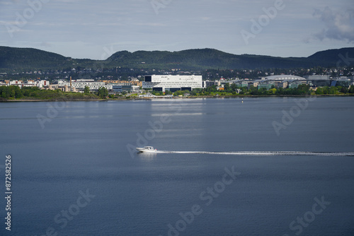 Photography A small boat travels across the calm waters of the Oslofjord in front of the Fornebu peninsula