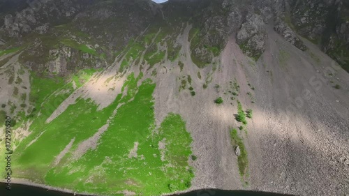 Steep mountainside screes tumbling down to dark lake with sunlight patches moving across screes. The Screes, Wastwater, Wasdale, Lake District, Cumbria, England, UK photo