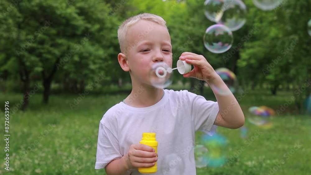 Cheerful blond boy blowing soap bubbles outdoors in the park in summer. Cheerful blond boy blowing soap bubbles outdoors in the park in summer.