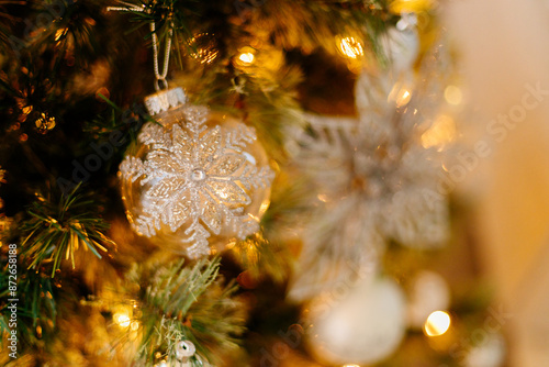 Bright white and silver ornamernts on Christmas tree against a background of bokeh of Christmas lights. New Year, Christmas background. Christmas tree, boxes with gifts,New year's figurines and decor