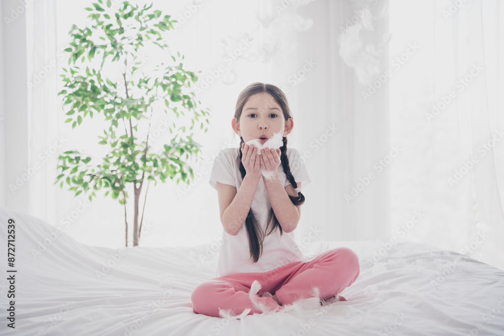 Full body portrait of adorable small girl blow air feather wear pajama comfy bed bedroom apartment indoors