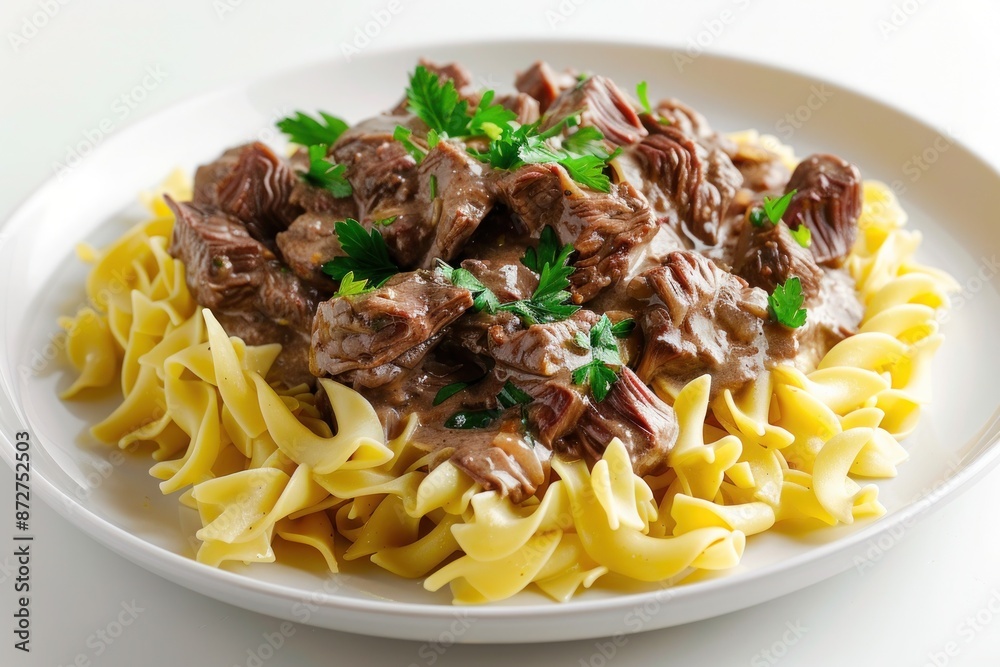 A plate of tender beef stroganoff served over egg noodles and garnished with parsley. Isolated on pure white background A plate of tender beef stroganoff served over egg noodles and garnished with parsley. Isolated on pure white background