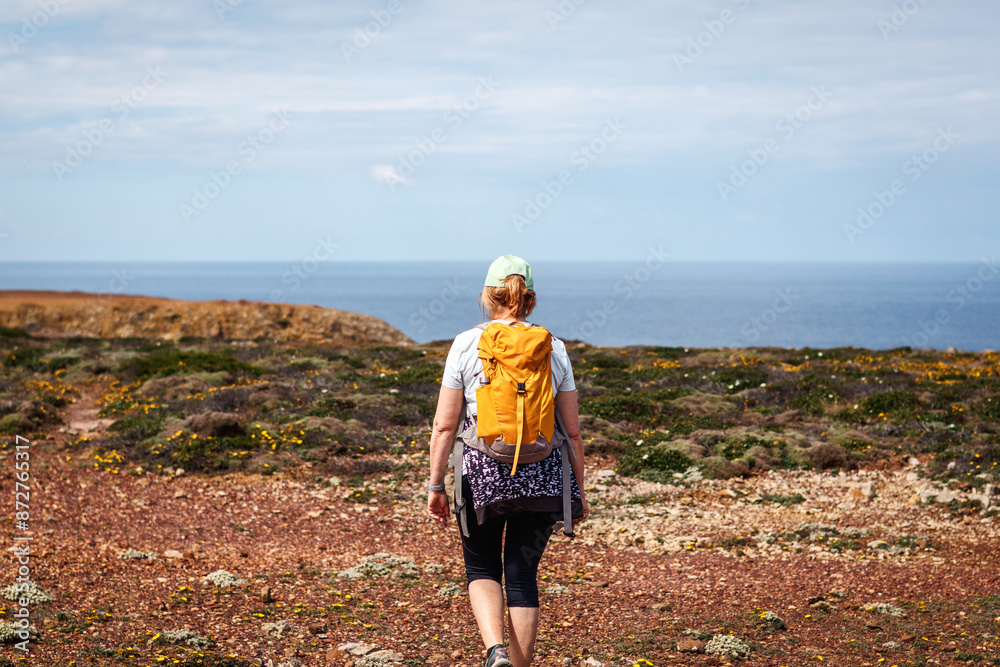 Woman with backpack walking at cliffs on Algarve coastline in Portugal. Active summer hiking vacation Woman with backpack walking at cliffs on Algarve coastline in Portugal. Active summer hiking vacation