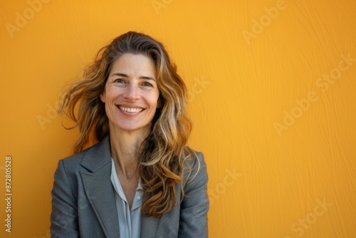 Portrait of a smiling woman in her 40s wearing a professional suit jacket over pastel orange background