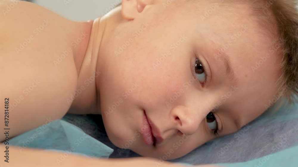 Cute boy lying on massage table having lymphatic drainage massage of body. Portrait of boy is lying on hospital bed waiting for medical procedure Cute boy lying on massage table having lymphatic drainage massage of body. Portrait of boy is lying on hospital bed waiting for medical procedure