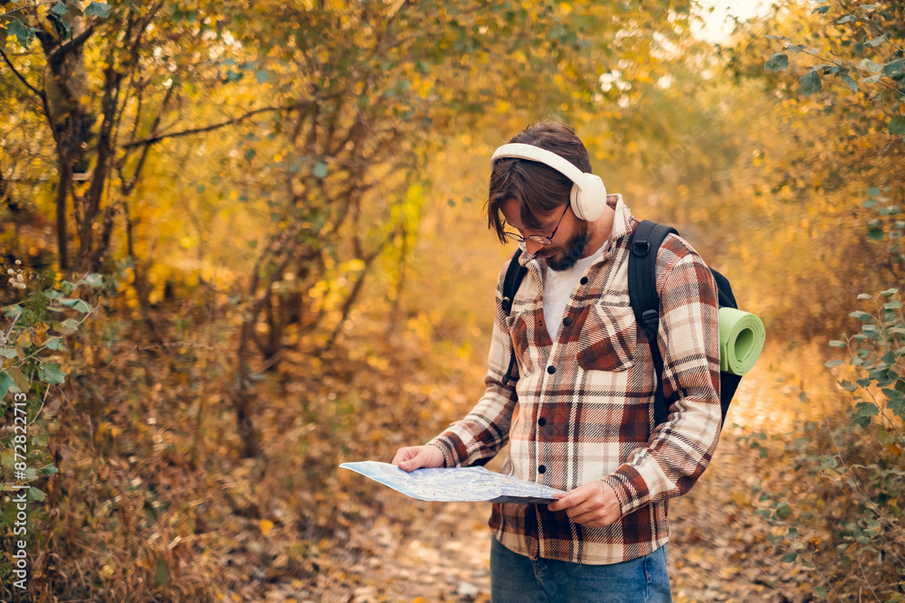 Profile view of man wearing glasses, studying map to navigate outdoor environment with backpack, emphasizing use of maps and navigation in nature. Profile view of man wearing glasses, studying map to navigate outdoor environment with backpack, emphasizing use of maps and navigation in nature.