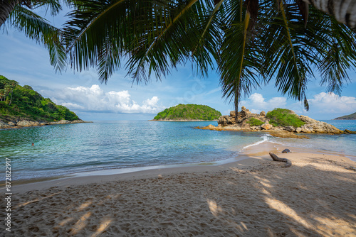 Blue sky over a small island surrounded by blue sea. White beach dotted with coconut trees. Yanui Beach, a viewpoint next to Promthep Cape and windmills, is a small beach with a split sea. photo