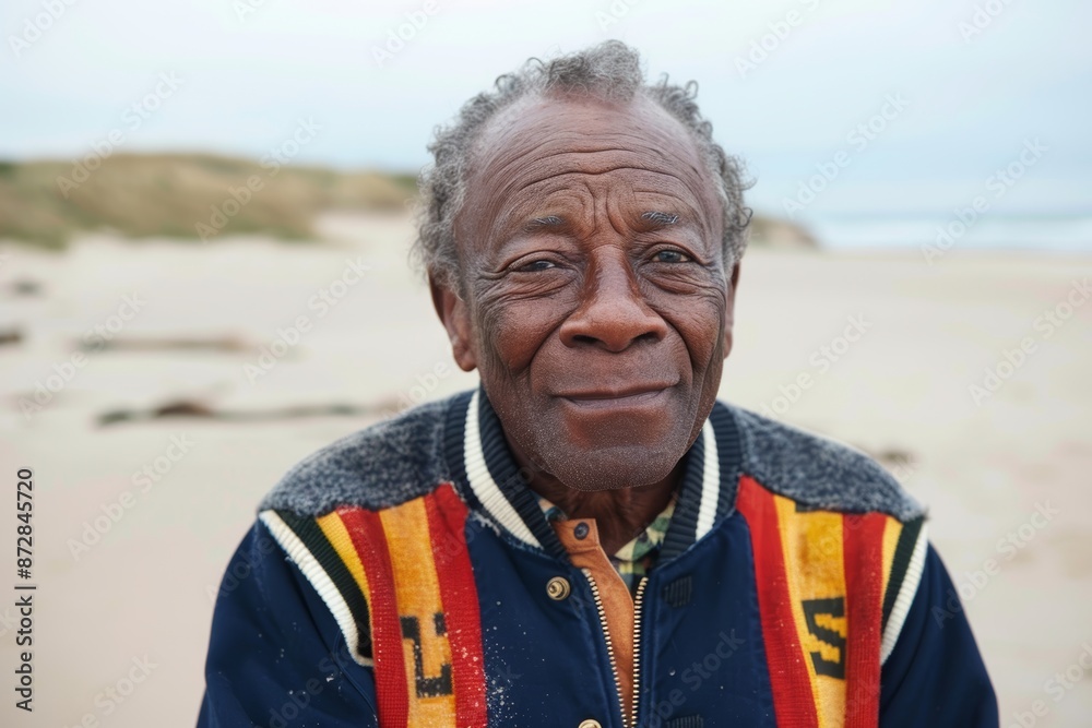 Portrait of a glad afro-american man in his 60s sporting a stylish varsity jacket in sandy beach background Portrait of a glad afro-american man in his 60s sporting a stylish varsity jacket in sandy beach background