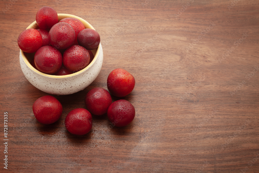 Top view of fresh Cherry Plum (Prunus cerasifera) fruits in a ceramic bowl, on a wooden background. Top view of fresh Cherry Plum (Prunus cerasifera) fruits in a ceramic bowl, on a wooden background.