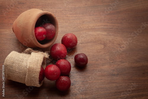 Top view of fresh Cherry Plum (Prunus cerasifera) fruits spilled out from a jute bag and a mud pot, on a wooden background.