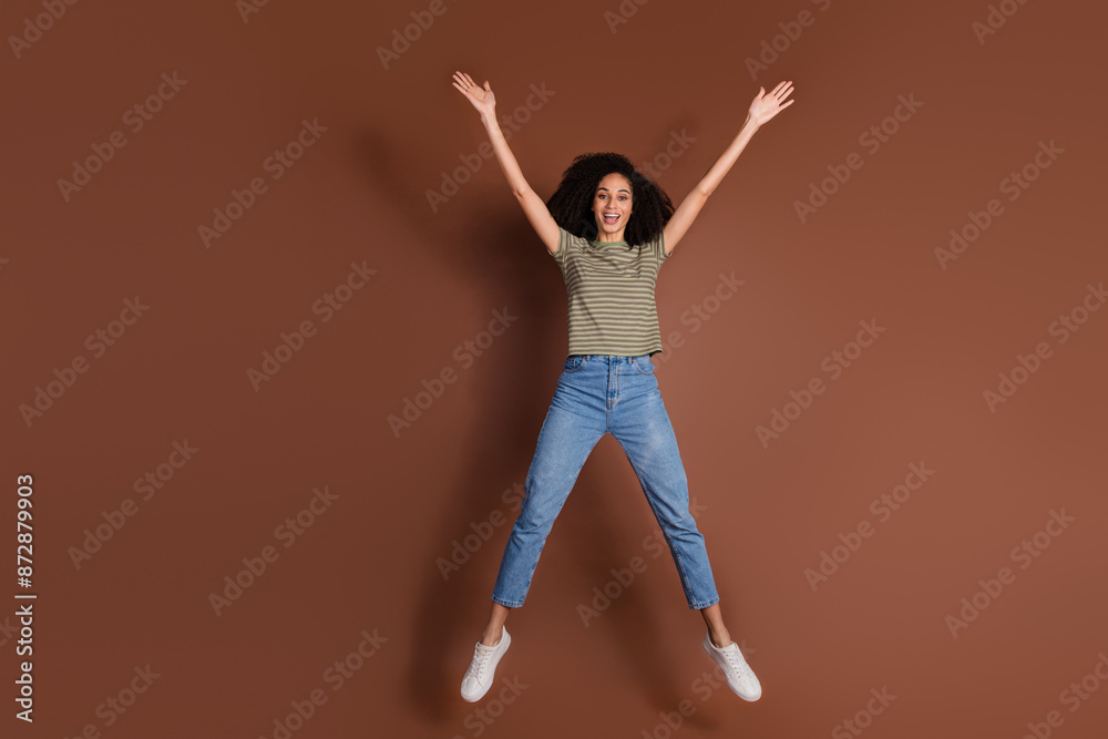 Full length photo of shiny attractive lady dressed striped t-shirt jumping high like star empty space isolated brown color background Full length photo of shiny attractive lady dressed striped t-shirt jumping high like star empty space isolated brown color background