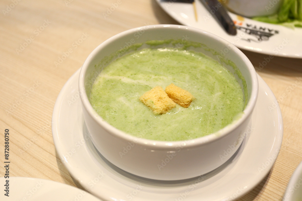 Green spinach soup in a white bowl with a saucer on the dining table.