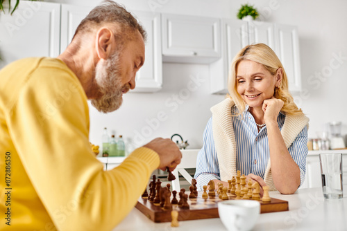 A mature loving couple in cozy homewear engage in a strategic game of chess, focused and immersed in the competition.