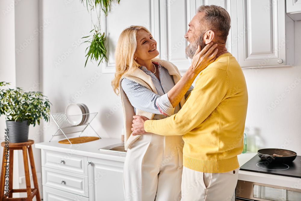 A mature loving couple in cozy homewear standing together in their kitchen, enjoying quality time together. A mature loving couple in cozy homewear standing together in their kitchen, enjoying quality time together.