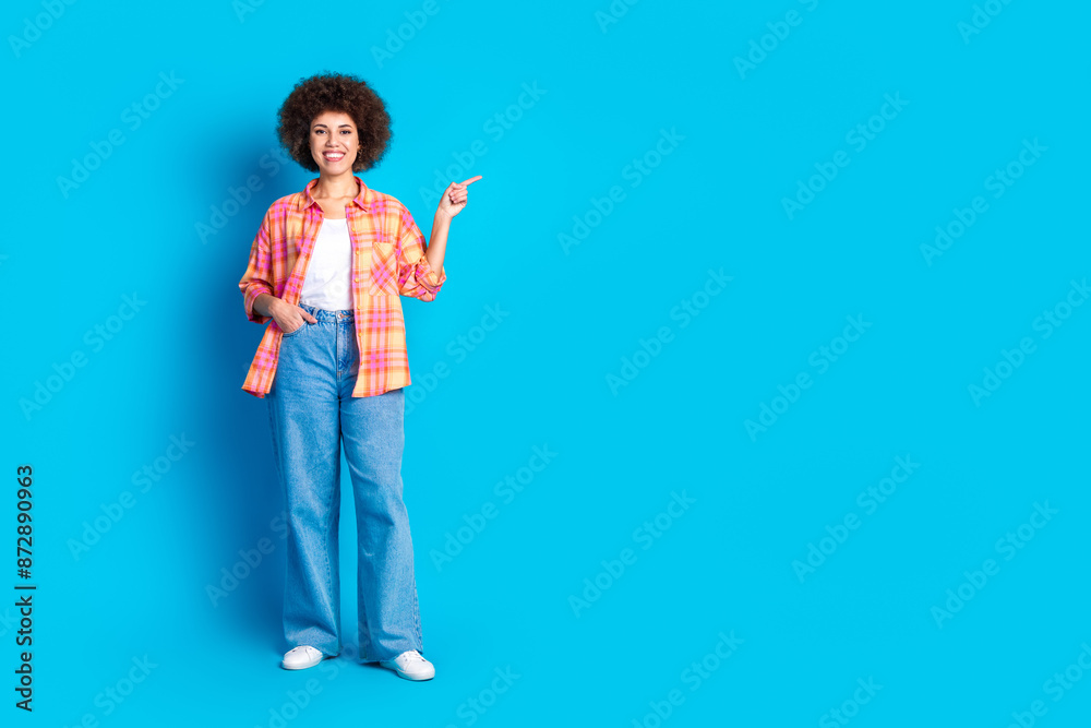 Full length photo of lovely young lady point empty space dressed stylish checkered garment isolated on blue color background Full length photo of lovely young lady point empty space dressed stylish checkered garment isolated on blue color background