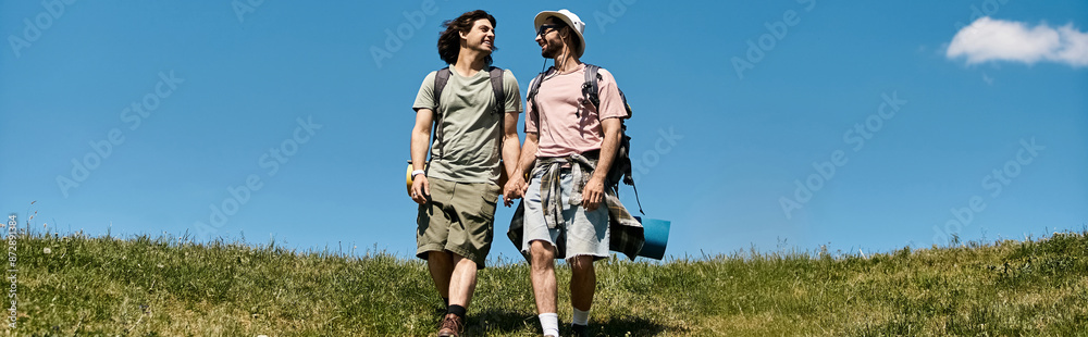 Two young men, a gay couple, hike together in a beautiful summer landscape, holding hands and enjoying the outdoors. Two young men, a gay couple, hike together in a beautiful summer landscape, holding hands and enjoying the outdoors.