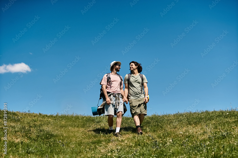 Two young men hike together in a beautiful, grassy landscape on a sunny day. Two young men hike together in a beautiful, grassy landscape on a sunny day.