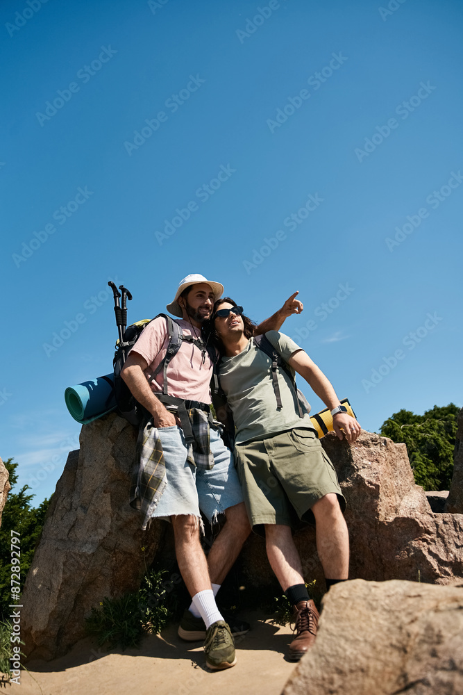 Obraz premium A gay couple hikes together through nature on a sunny summer day, enjoying the view from a rocky overlook.