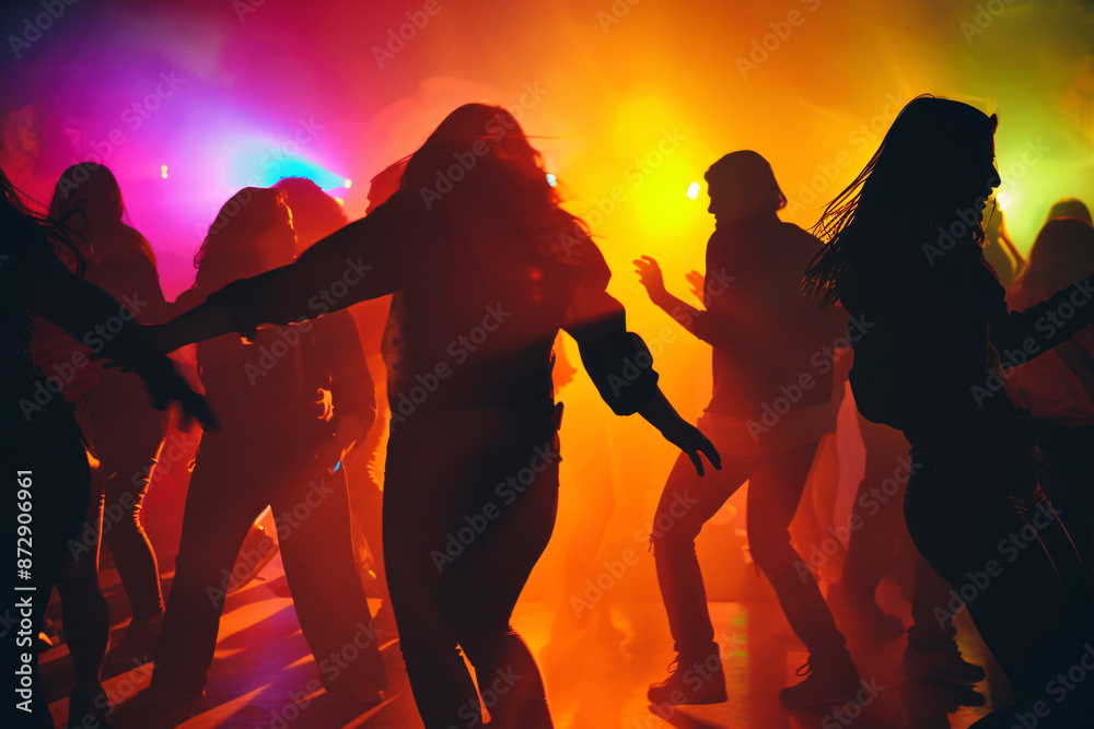 Fototapeta premium Silhouettes of people dancing in a colorful and vibrant party atmosphere with bright lights creating an energetic and lively scene