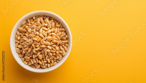 Bowl with wheat grains on empty yellow background. Close-up. Top view, flat lay. Space for text.