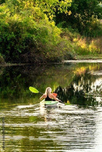 Woman kayaking on a serene river surrounded by lush greenery during a sunny day