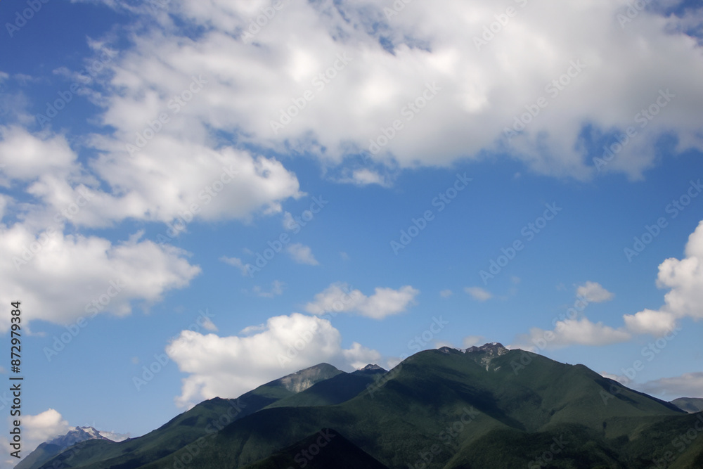 Fototapeta premium Mountains in nature with blue sky. Mountain travel green concept. Clouds in the sky over mountains in nature. Mountains and clouds in a blue sky lifestyle with nature.