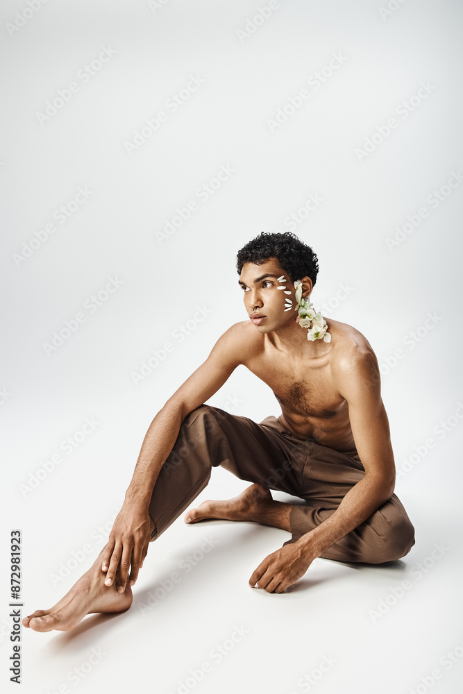 A young, muscular African American man adorned with flowers poses on a grey background. A young, muscular African American man adorned with flowers poses on a grey background.
