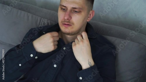 A man sits on the sofa and suffers from the heat.
The room is very hot, the man waves his hands to cool down a little.
A man tries to freshen up in a stuffy room