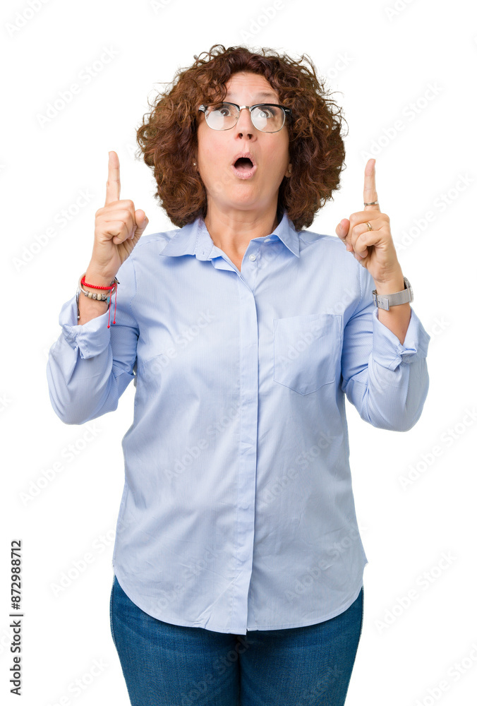 Beautiful middle ager senior businees woman wearing glasses over isolated background amazed and surprised looking up and pointing with fingers and raised arms. Beautiful middle ager senior businees woman wearing glasses over isolated background amazed and surprised looking up and pointing with fingers and raised arms.