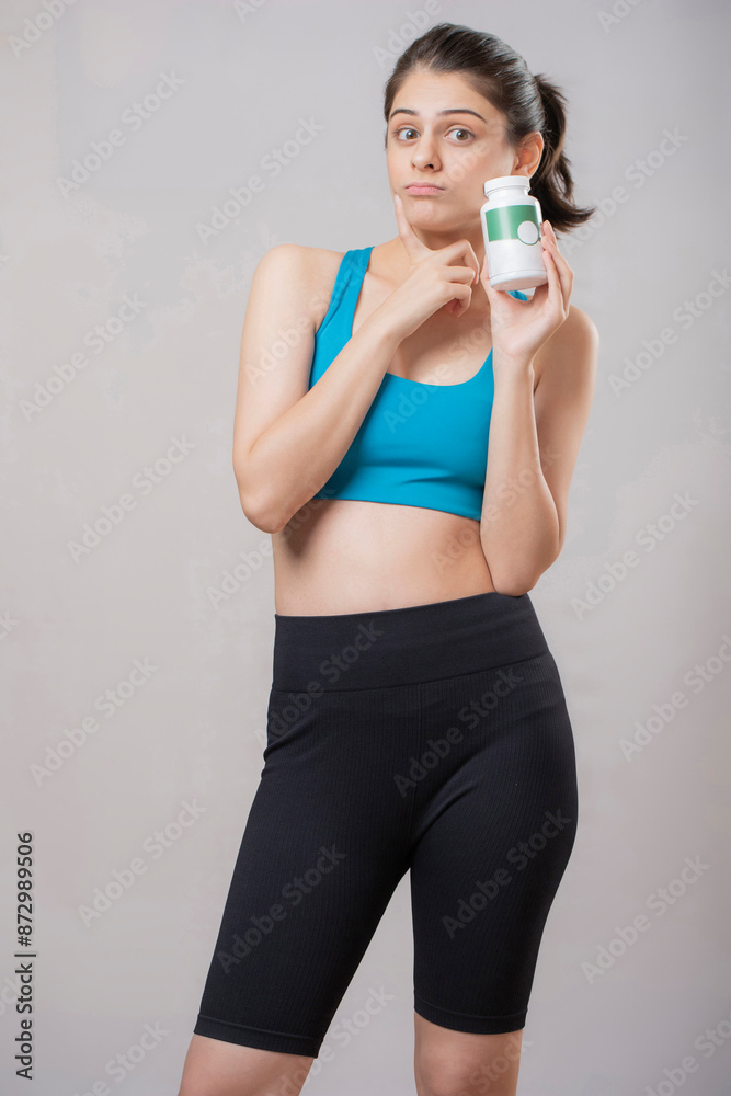 Beautiful Woman In Yoga Pants With A Confused Expression While Holding Medicine Bottle Beautiful Woman In Yoga Pants With A Confused Expression While Holding Medicine Bottle