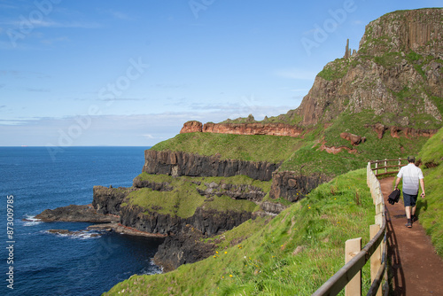 A man walking on a pathway at Giants Causeway, Northern Ireland. Blue sky and mountains photo