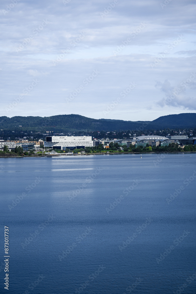 A distant view of Fornebu, a peninsula in Norway on the Oslofjord. The shot captures a cityscape with residential area including large, modern office buildings and a Stadium. A distant view of Fornebu, a peninsula in Norway on the Oslofjord. The shot captures a cityscape with residential area including large, modern office buildings and a Stadium.