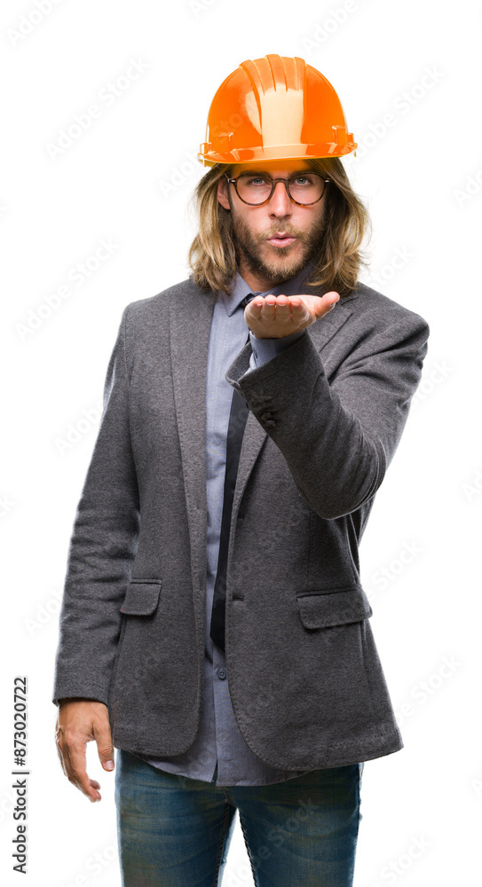 Young handsome architec man with long hair wearing safety helmet over isolated background looking at the camera blowing a kiss with hand on air being lovely and sexy. Love expression. Young handsome architec man with long hair wearing safety helmet over isolated background looking at the camera blowing a kiss with hand on air being lovely and sexy. Love expression.
