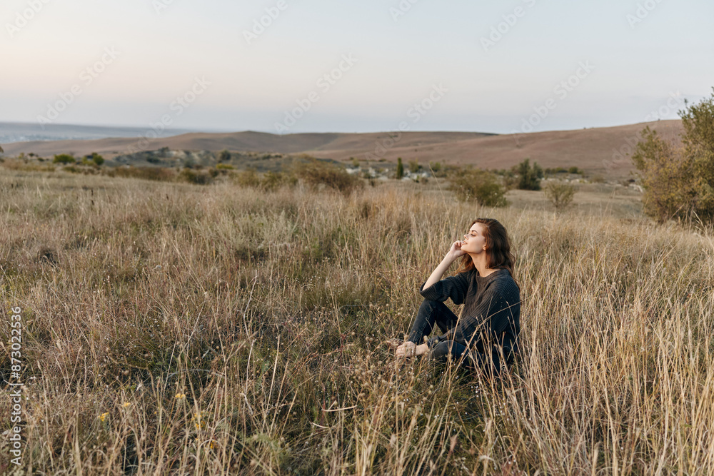 Woman relaxing in tall grass on hill during sunset in field Woman relaxing in tall grass on hill during sunset in field