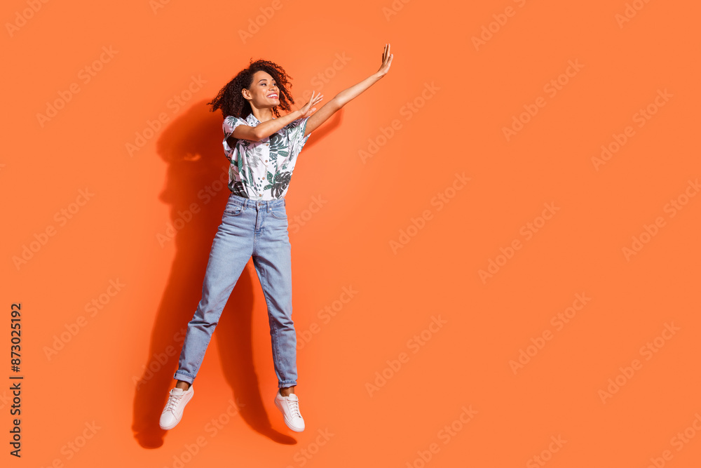 Full body photo of american woman in jeans and hawaiian shirt jumping looking empty space grabbing product isolated on orange color background Full body photo of american woman in jeans and hawaiian shirt jumping looking empty space grabbing product isolated on orange color background