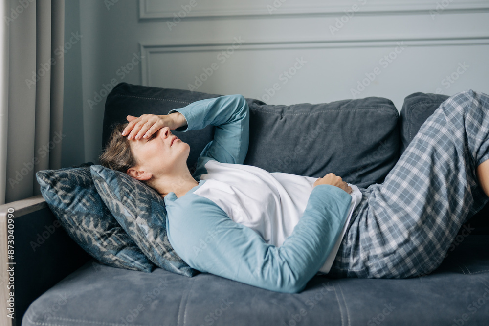 A stressed woman with a migraine lies on the sofa at home, covering her face with her hand. A stressed woman with a migraine lies on the sofa at home, covering her face with her hand.