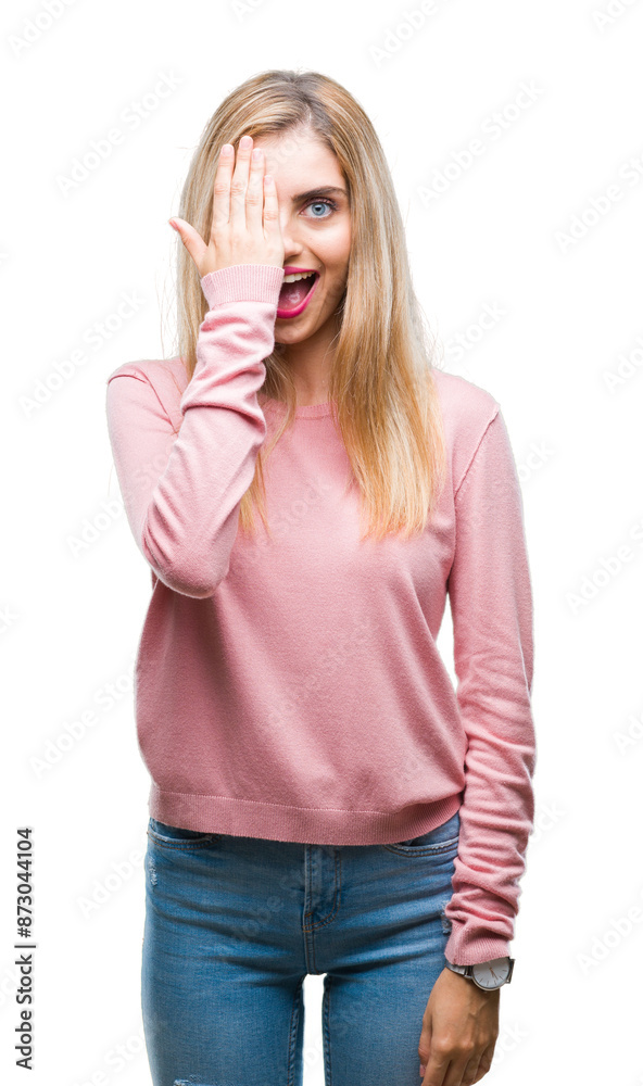 Young beautiful blonde woman wearing pink winter sweater over isolated background covering one eye with hand with confident smile on face and surprise emotion.