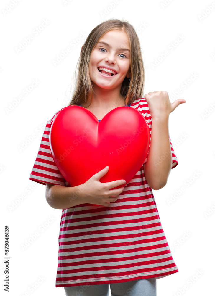 Young beautiful girl holding red heart over isolated background pointing and showing with thumb up to the side with happy face smiling Young beautiful girl holding red heart over isolated background pointing and showing with thumb up to the side with happy face smiling