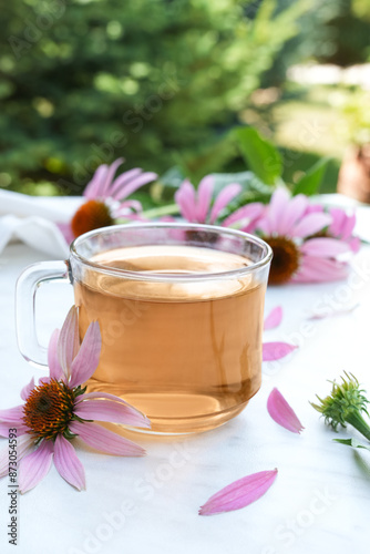 Cup of healthy echinacea tea, fresh coneflower herbs on a light table. Side view.