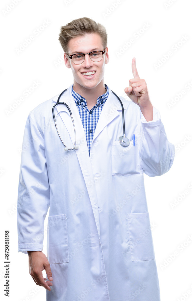 Young handsome blond doctor surprised with an idea or question pointing finger with happy face, number one