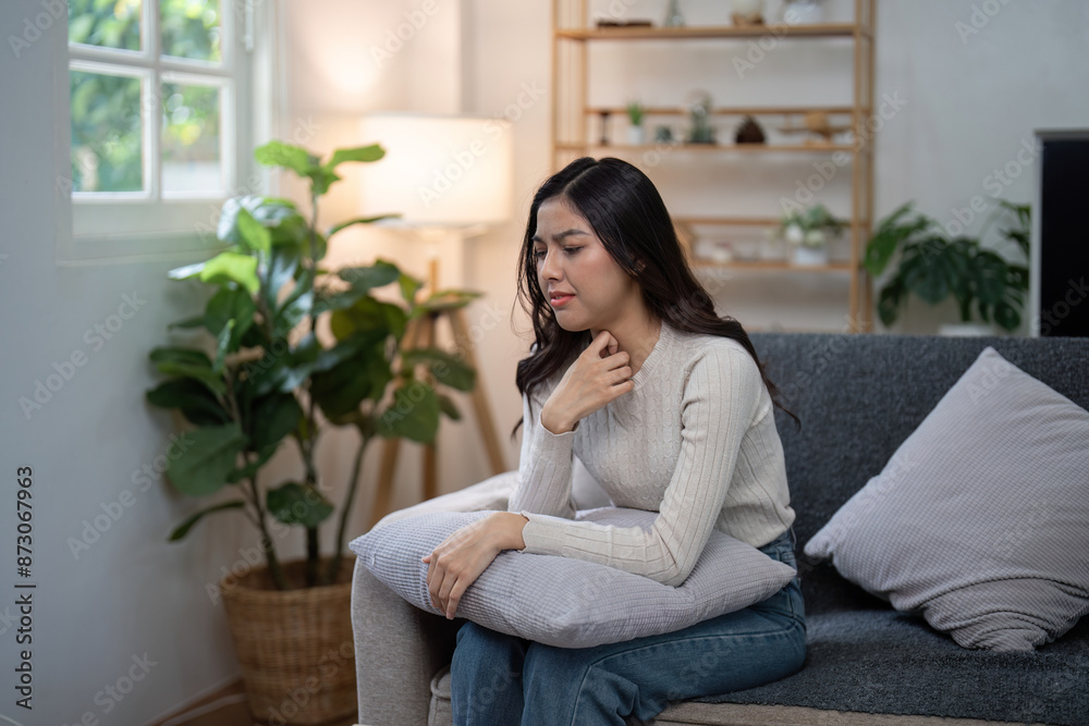 Young Woman Experiencing Discomfort at Home, Sitting on Couch and Holding Pillow, healthcare and Wellness Concept Young Woman Experiencing Discomfort at Home, Sitting on Couch and Holding Pillow, healthcare and Wellness Concept
