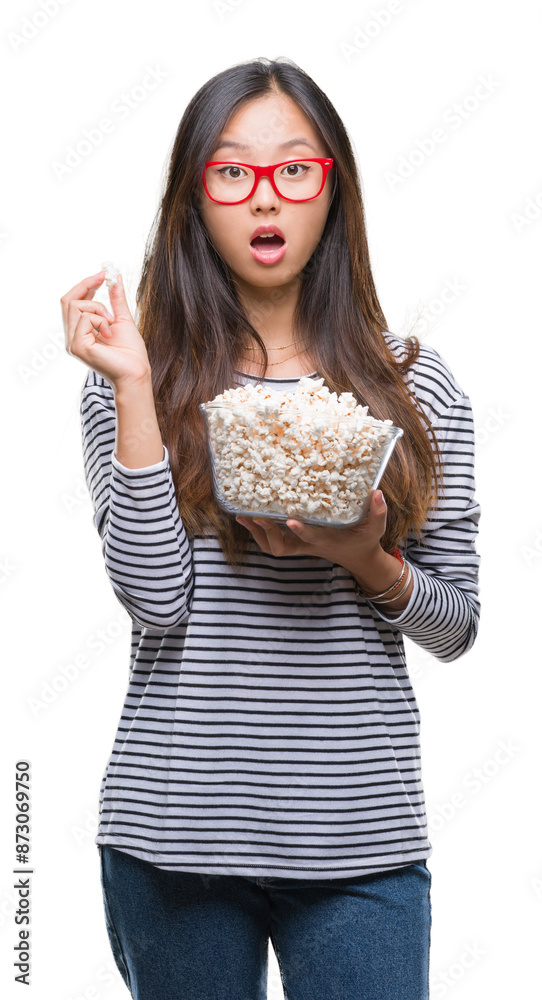 Young asian woman eating popcorn over isolated background scared in shock with a surprise face, afraid and excited with fear expression Young asian woman eating popcorn over isolated background scared in shock with a surprise face, afraid and excited with fear expression