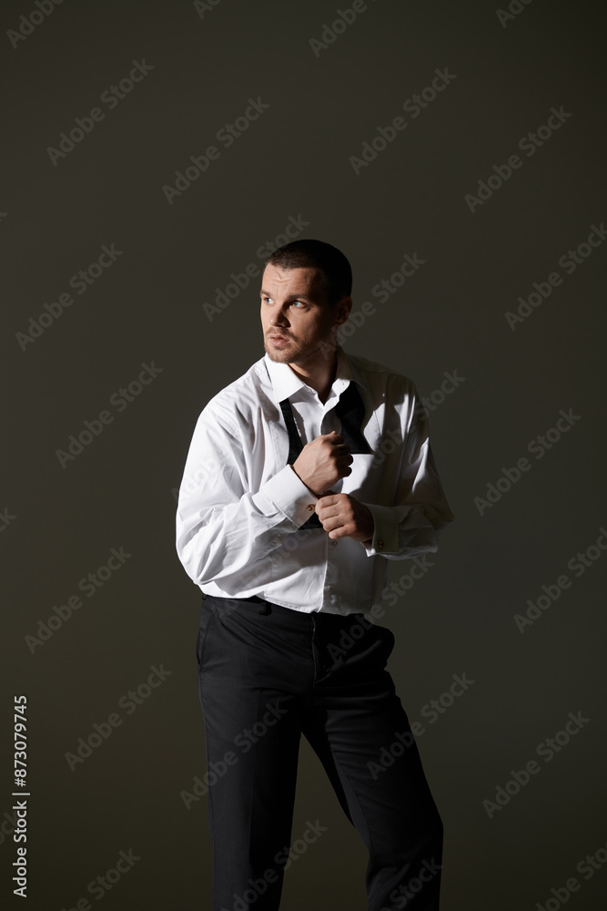 Man adjusts bowtie dramatically against gray background. Man adjusts bowtie dramatically against gray background.