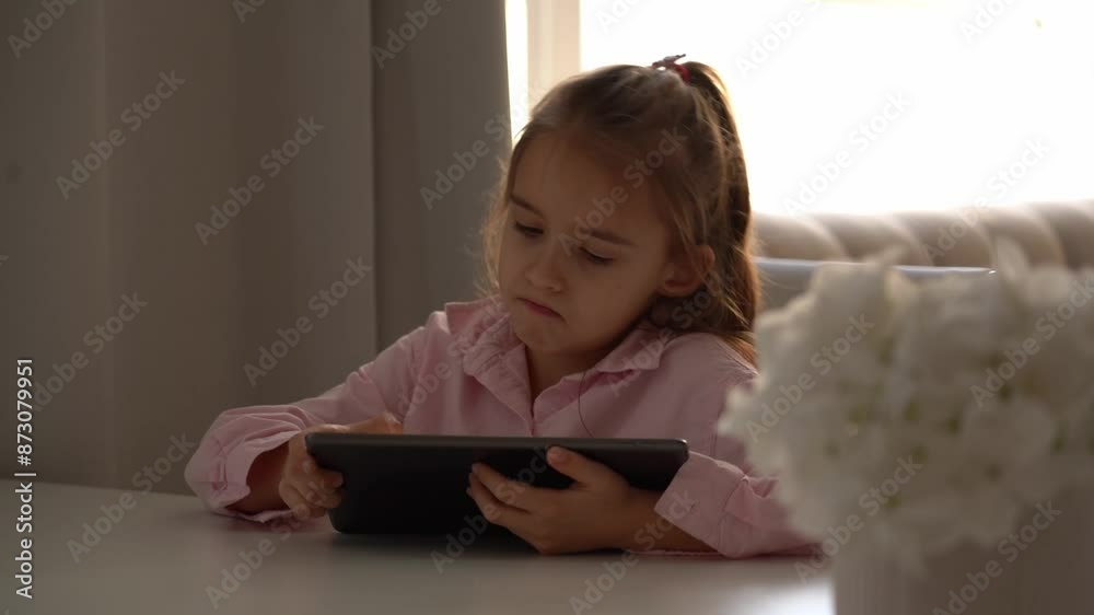 Upset Girl Using Tablet. Intensely focused on a gadget. Caucasian school girl Engaged With Tablet in Bright Living Room During Daytime Upset Girl Using Tablet. Intensely focused on a gadget. Caucasian school girl Engaged With Tablet in Bright Living Room During Daytime