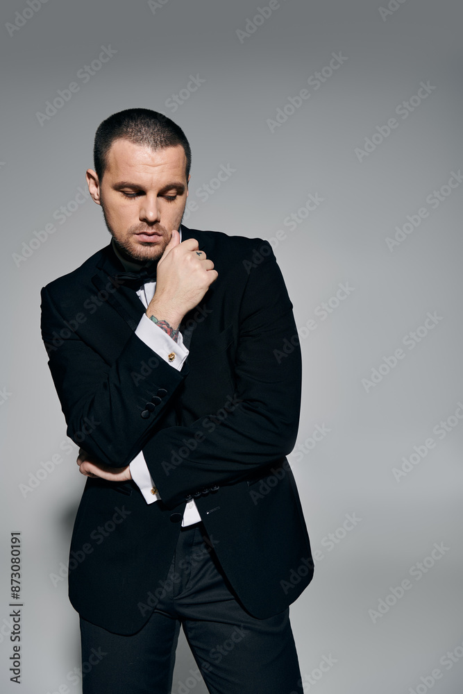 A man in a tuxedo stands in a studio, thoughtfully touching his chin. A man in a tuxedo stands in a studio, thoughtfully touching his chin.