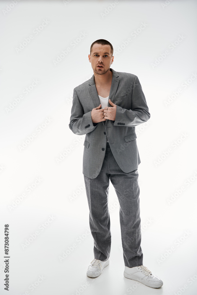 A stylish man in a grey suit stands with his jacket open, looking directly at the camera. A stylish man in a grey suit stands with his jacket open, looking directly at the camera.