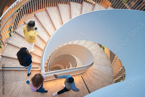High angle view of colleagues moving up on spiral staircase in office