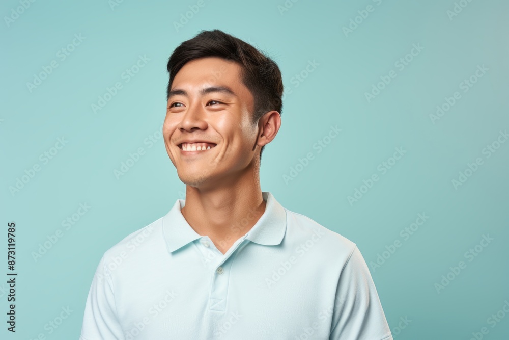 Portrait of a smiling asian man in his 20s wearing a breathable golf polo isolated on pastel blue background Portrait of a smiling asian man in his 20s wearing a breathable golf polo isolated on pastel blue background