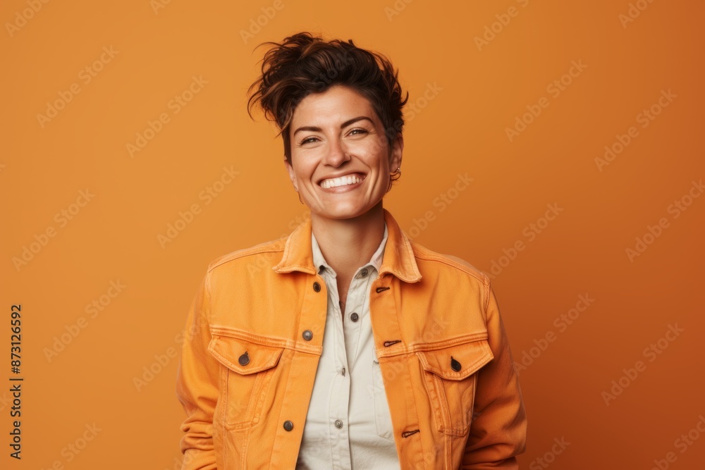 Portrait of a cheerful woman in her 40s wearing a rugged jean vest isolated on pastel orange background Portrait of a cheerful woman in her 40s wearing a rugged jean vest isolated on pastel orange background