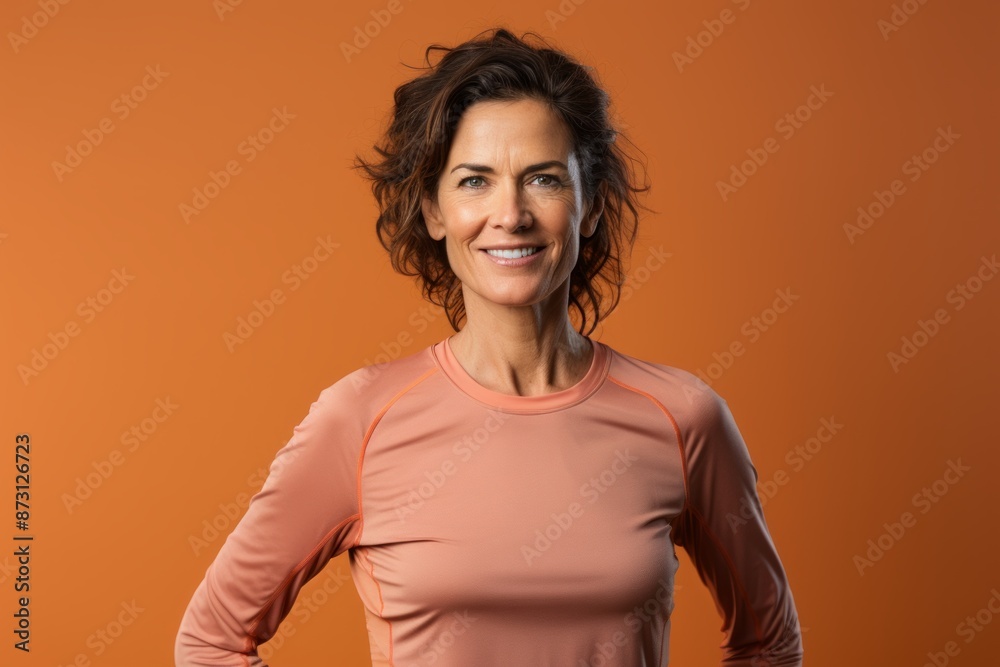 Obraz premium Portrait of a tender woman in her 40s wearing a moisture-wicking running shirt isolated on pastel orange background